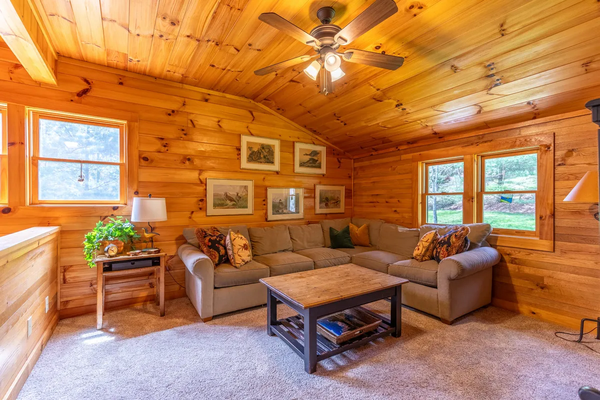 A spacious, welcoming living room with a comfortable sectional sofa, a wooden coffee table, and framed artwork on the walls. The mood is cozy and communal, offering places to read, relax, or share warm drinks.