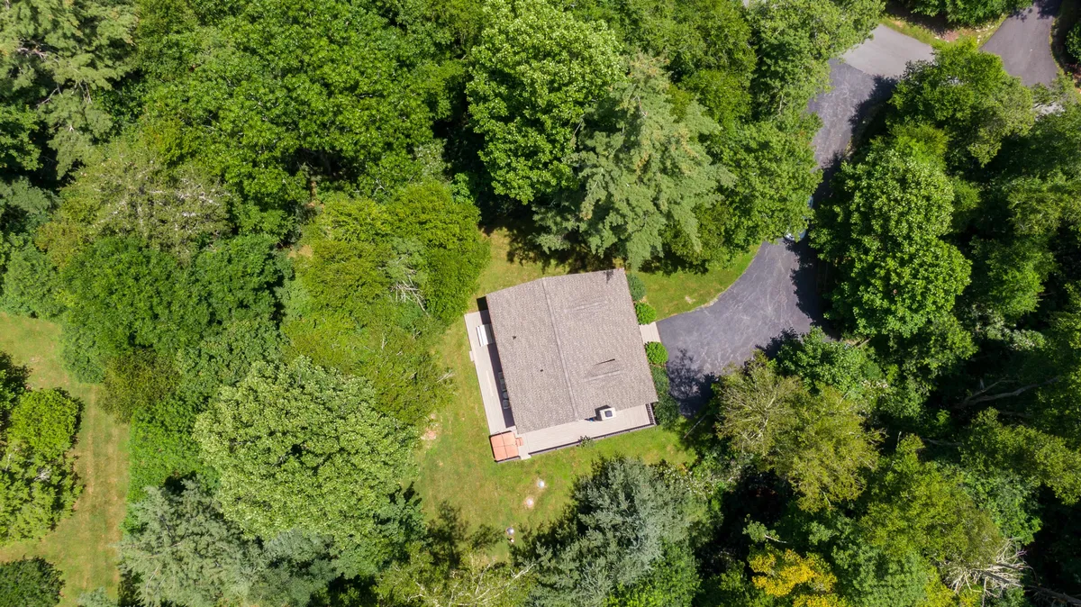 A view of the property nestled among mature trees, showing the house, surrounding greenery, and a driveway. This broad perspective situates the home in a tranquil, wooded environment, suggesting easy access to regional adventure and immersion in natural beauty.