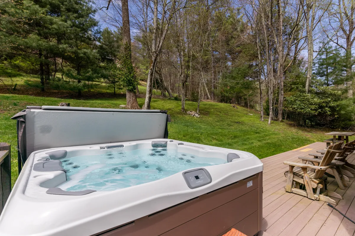 This image features a tranquil outdoor hot tub set on a spacious deck, surrounded by lush evergreens. The setting is private and immersed in nature, perfect for relaxing together. The scene captures the soft natural light filtering through the trees, emphasizing a peaceful and romantic atmosphere.