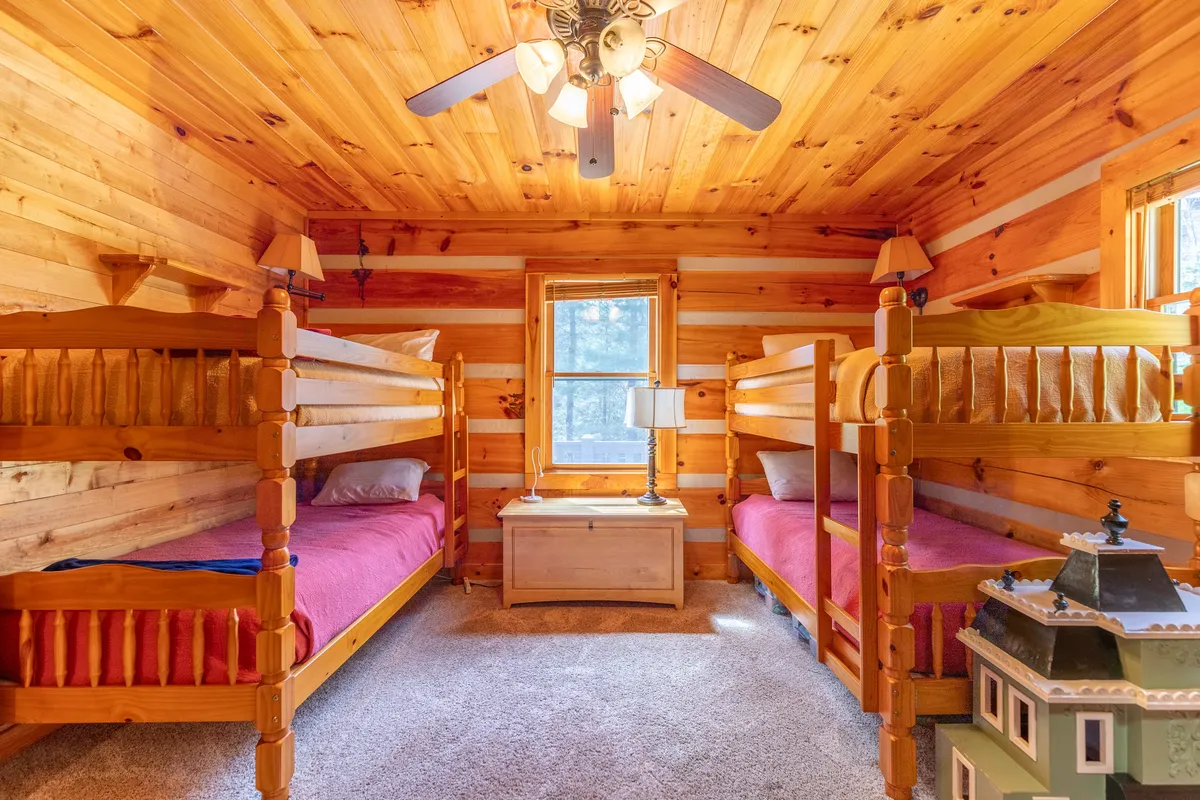 The image shows a cheerful bunk room with two sturdy bunk beds, a window allowing natural light to brighten the space, a lamp for nighttime reading, and a chest of drawers for storage. The bedding and decor create a playful and welcoming atmosphere ideal for children or families.