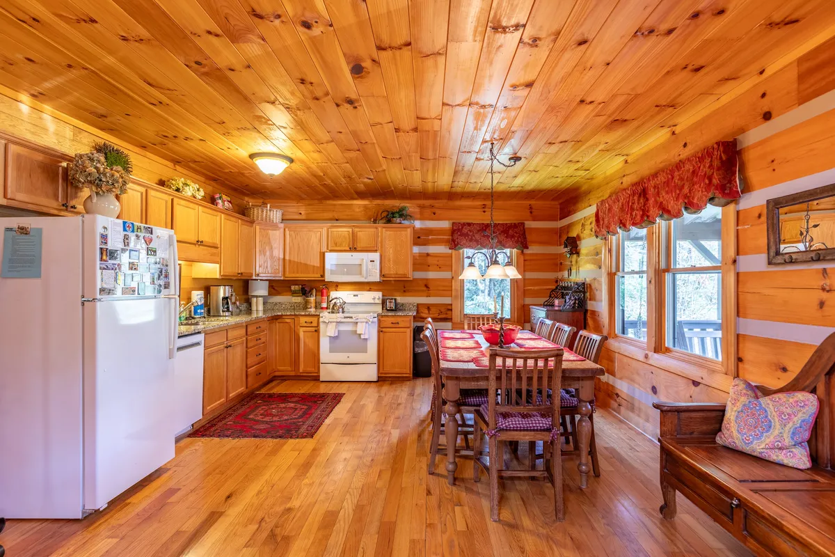 A view of the kitchen and dining area featuring a kitchen island, wooden cabinetry, large windows, and a welcoming dining table. The setup is designed for both cooking and socializing, with ample space for family feasts or group cooking sessions.