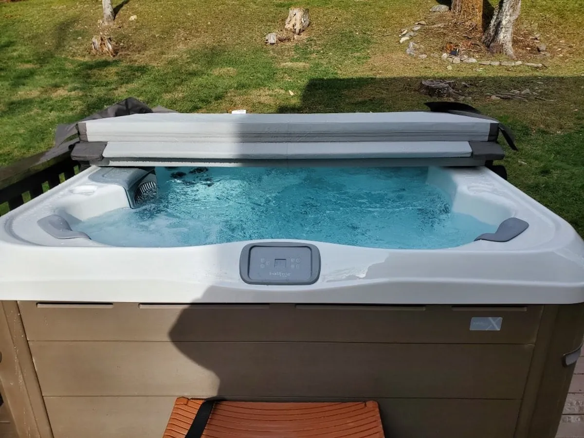A tranquil outdoor hot tub set on a wooden deck, surrounded by lush evergreens. The scene captures the hot tub as the main focal point, with ample space for relaxing. Warm sunset tones bathe the area, inviting users to unwind amidst nature.