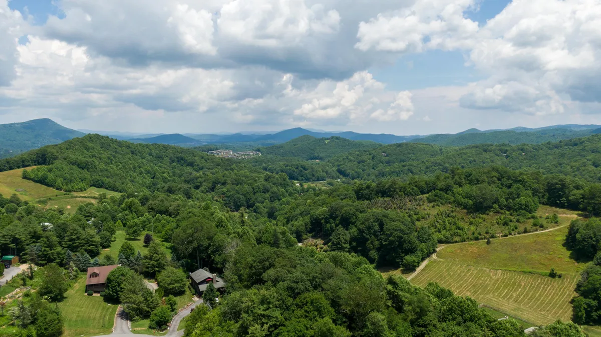 A sweeping view of rolling hills, dense forest, and distant mountains with a few scattered homes. The vista captures the natural beauty and secluded setting of the area, evoking the sense of exploring and discovering the local landscape and attractions nearby.